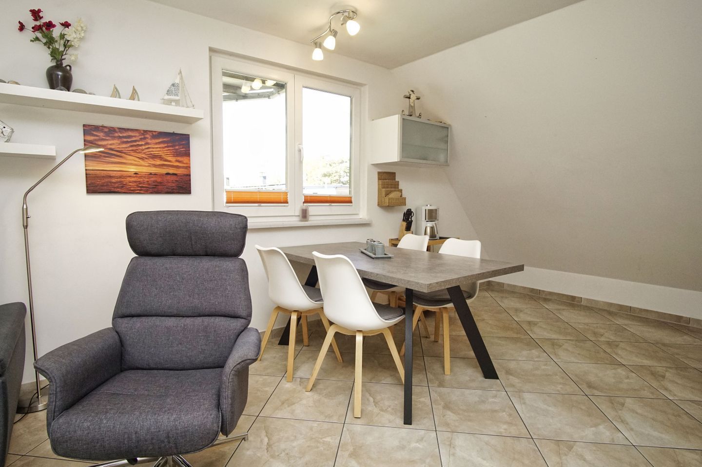 A modern dining area with a grey upholstered chair, white chairs, and a grey table.