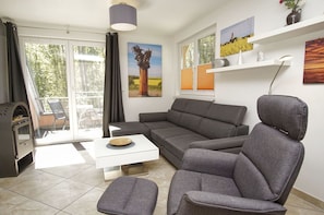 A modern living room with a grey sofa, a white coffee table, and a grey ottoman. There is a fireplace on the left, a window with blinds, and a painting on the wall.