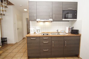 A compact kitchen with dark wood cabinets, a stainless steel sink, and a built-in microwave. - Near the famous cape, a beautiful sandy beach - Ferienresidenz Kap Arkona FeWo 06 - (Putgarten)