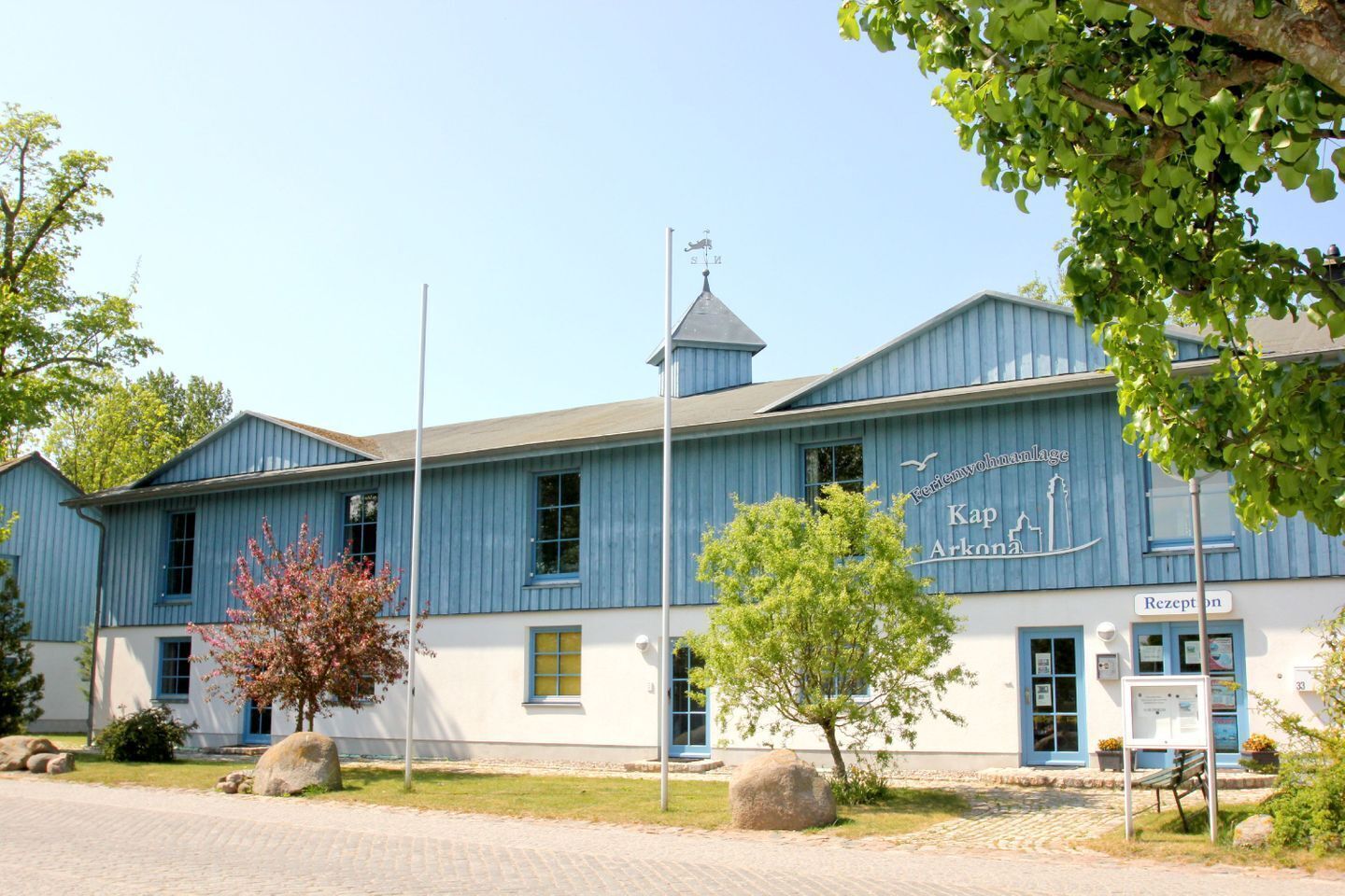 Un bâtiment à la façade bleue, surmonté d’une girouette et portant une enseigne indiquant « Friedenswohllage Kap Arkona ».