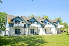 A row of blue and white buildings with multiple balconies, a grassy lawn, and a clear sky.