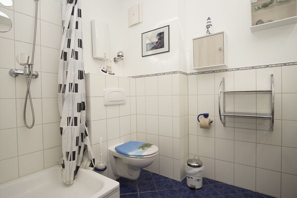 A bathroom with a shower, toilet, and sink. There is a towel rack and a small trash can.