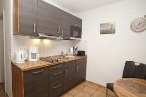 A compact kitchen with dark cabinets, a microwave, a coffee maker, and a sink.