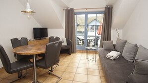 A modern living room with a dining area, a sofa, a TV, and a balcony with curtains. - Close to the famous cape, beautiful sandy beach - Ferienresidenz Kap Arkona FeWo 06 - (Putgarten)