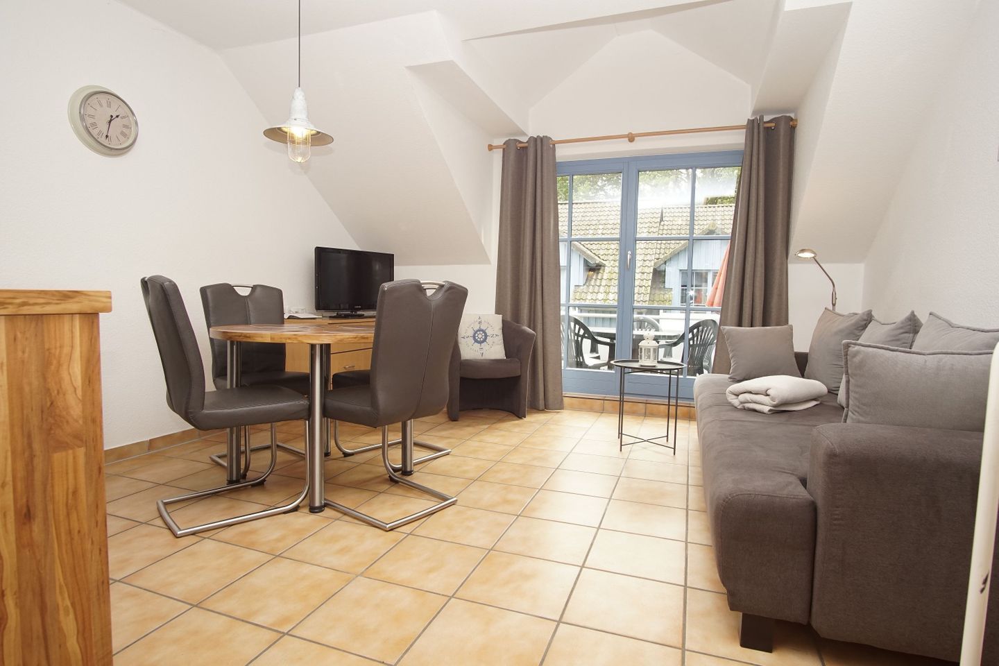 Una sala moderna con un sofá, una mesa de comedor con sillas, un televisor y una ventana con cortinas.