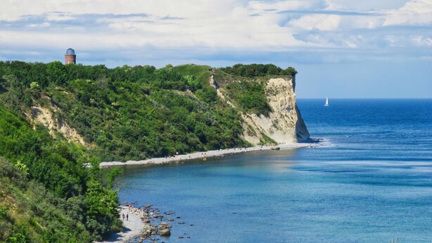 A coastal landscape with a lighthouse on a cliff, a beach, and a sailboat in the distance. - Close to the famous cape, beautiful sandy beach - Ferienresidenz Kap Arkona FeWo 06 - (Putgarten)