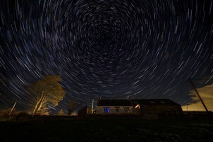 Fotografía de estelas de estrellas con una casa y un árbol en primer plano.
