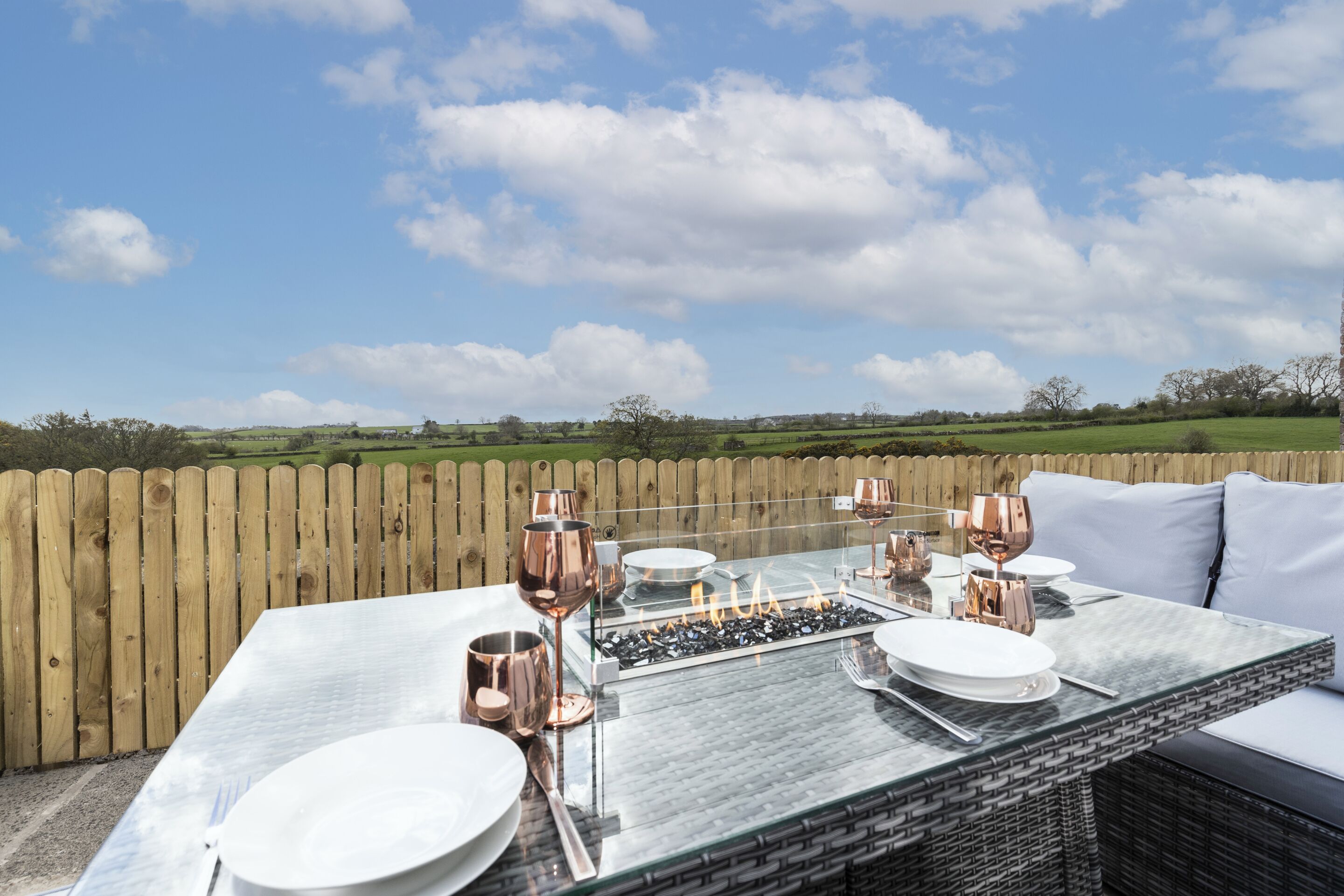 An outdoor dining area with a table set for two, surrounded by a wooden fence, under a clear sky.