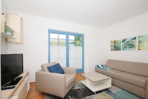 A modern living room with a TV, two sofas, a coffee table, and a sliding glass door.