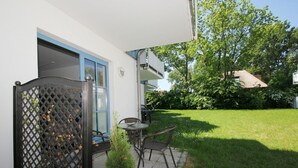 A patio with a table and chairs, a small garden, and a white building with a blue door.