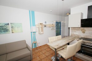 A compact kitchen with a dining table, chairs, a sofa, a floor lamp, and a microwave.