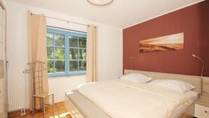 A bedroom with a bed, a window with curtains, a radiator, a bedside table, and a wall-mounted lamp.