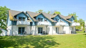 A row of blue and white buildings with multiple balconies, a grassy lawn, and a clear sky.