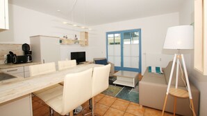 A modern, well-lit apartment with a dining area, kitchenette, and a large window with a blue door.