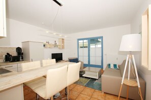 A modern, well-lit apartment with a dining area, kitchenette, and a large window with a blue door. - Close to the famous cape, beautiful sandy beach - Ferienresidenz Kap Arkona FeWo 12 - (Putgarten)