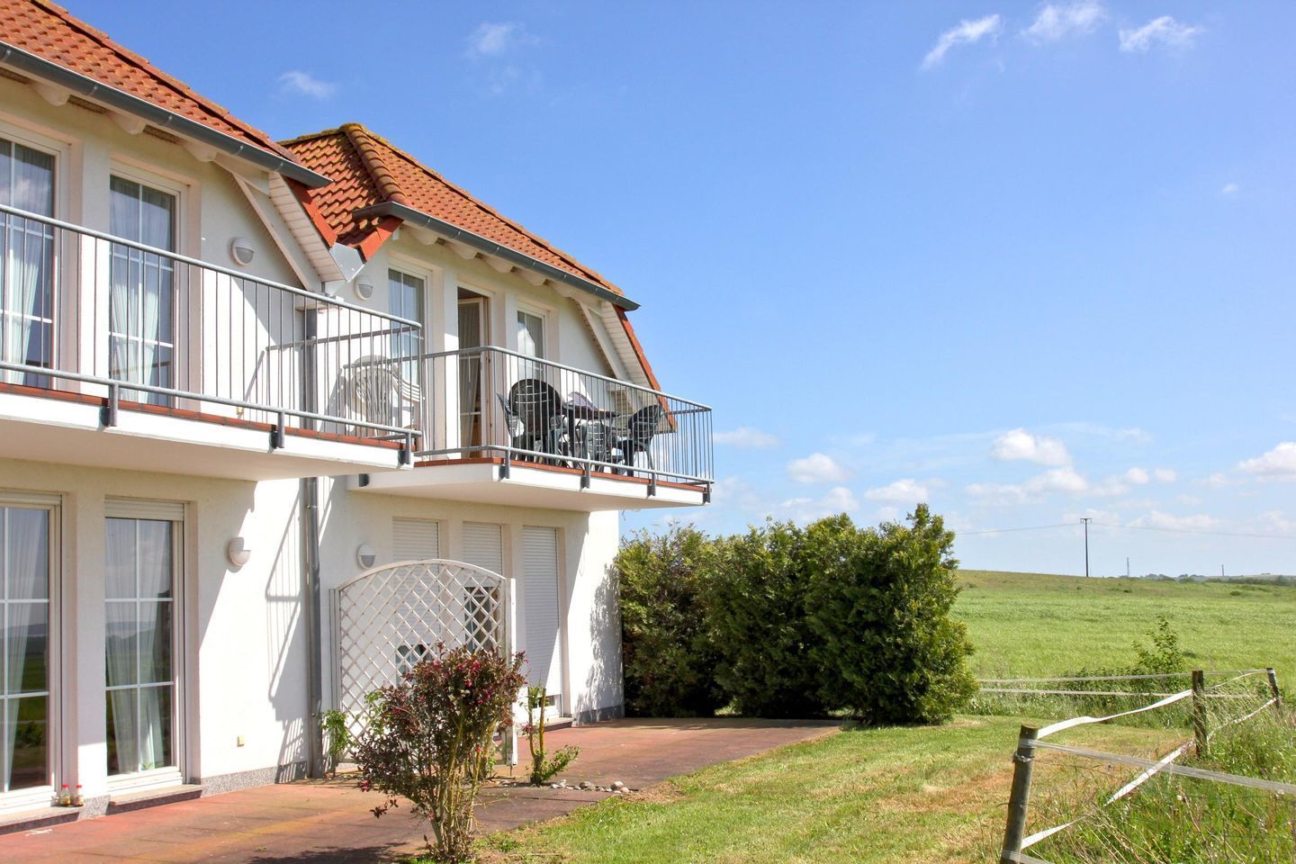 A two-story house with a balcony, large windows, and a well-maintained garden.