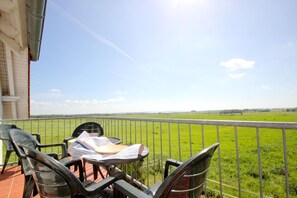 Un balcon avec une table et des chaises donnant sur un champ verdoyant.