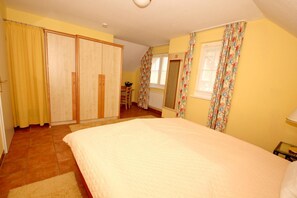 Une chambre à coucher avec un lit, une armoire, un miroir et une fenêtre avec des rideaux.