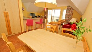 Ein Essbereich mit Holztisch und -stühlen, einem roten Sofa, einer großen Lampe und Blick ins Freie.