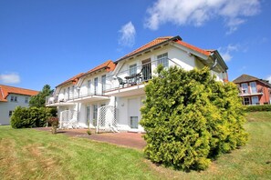 Un bâtiment à deux étages, doté d’un toit recouvert de tuiles rouges, de balcons avec des garde-corps et d’une pelouse bien entretenue.
