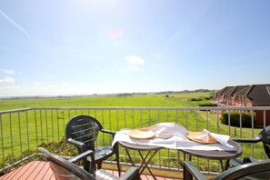 Une terrasse avec une table dressée pour deux personnes, donnant sur un champ verdoyant et une rangée de maisons.