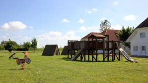 Ein Spielplatz mit Rutsche und Klettergerüsten, umgeben von einer grünen Wiese und einem Gebäude mit rotem Dach.