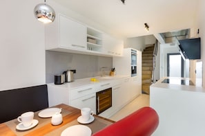 A modern kitchen with white cabinets, a built-in oven, and a dining area with a red chair and white tableware.