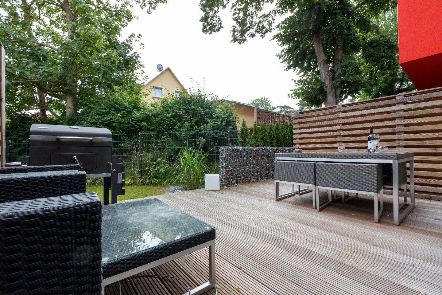 An outdoor patio with a grill, wicker furniture, and a table with glasses and a bottle.