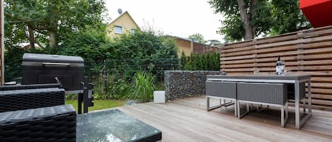 An outdoor patio with a grill, wicker furniture, and a table with glasses and a bottle.