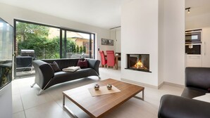A modern living room with a fireplace, a sofa, a coffee table, and a dining area with a red chair.