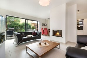 Una sala de estar moderna con chimenea, un sofá, una mesa de centro y un comedor con una silla roja.