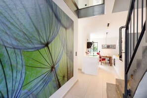 Un interior moderno con una escalera, una zona de comedor y un gran mural abstracto.