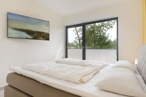 Een slaapkamer met een groot raam, een bed met wit beddengoed en een schilderij aan de muur.