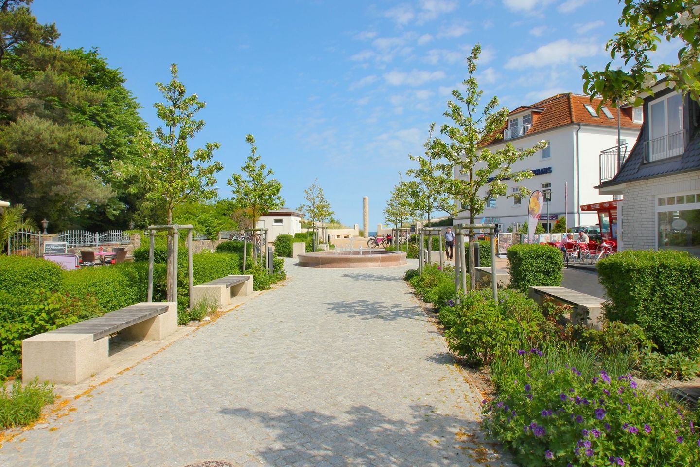 A paved pathway leading to a central plaza with benches and greenery.