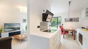 A modern kitchen with a central island, a dining area with a red chair, and a TV in the living room.