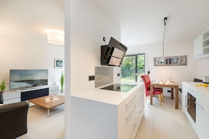 Una cocina moderna con una isla central, un comedor con una silla roja y un televisor en la sala de estar.