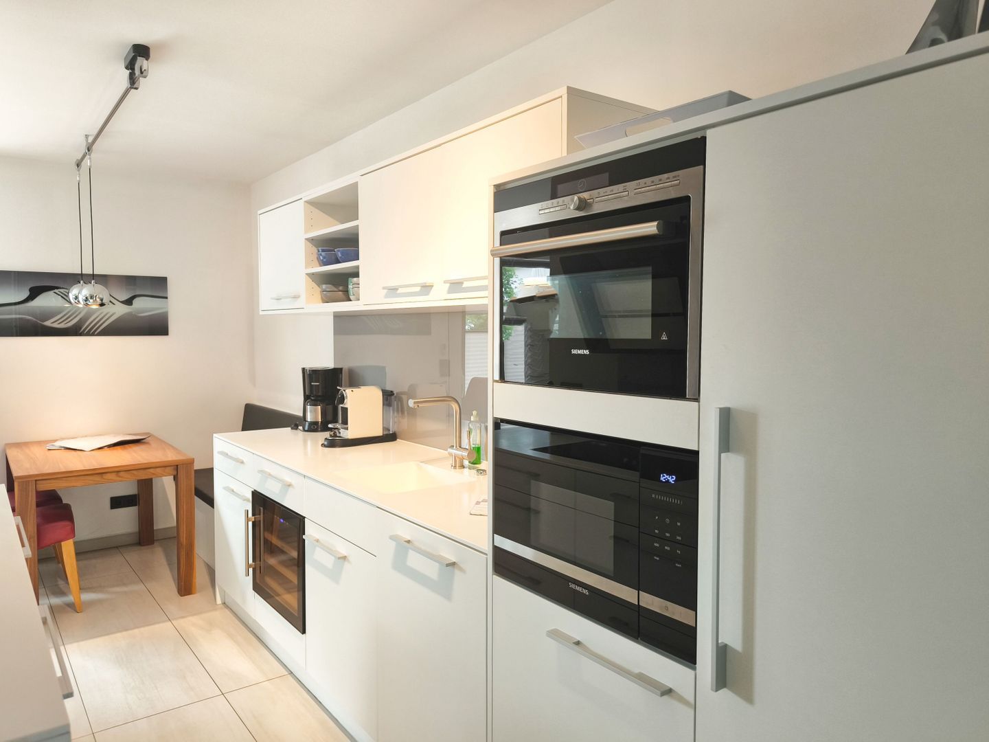 A modern kitchen with white cabinetry, a built-in oven, a microwave, and a coffee maker.