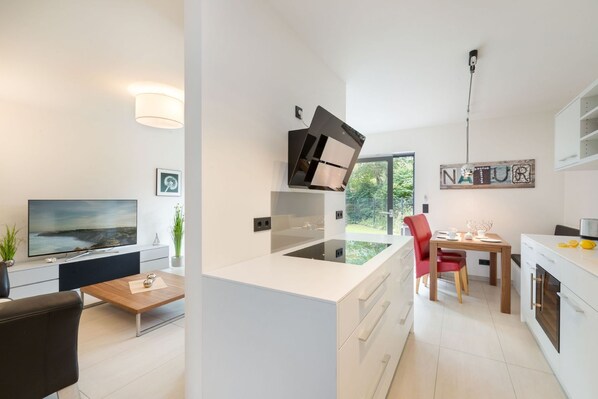 A modern kitchen with a central island, a dining area with a red chair, and a TV in the living room.