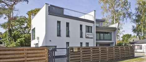 A modern two-story building with a white facade, large windows, and a balcony.