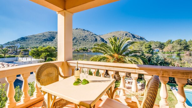 A balcony with a table and chairs, overlooking a lake and mountains. - House in Alcudia Aran Berna with swimming pool (Alcúdia)