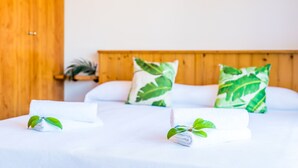 A neatly made bed with white linens and green leaf-patterned pillows, set against a wooden headboard and a plain white wall. - House in Alcudia Aran Berna with swimming pool (Alcúdia)
