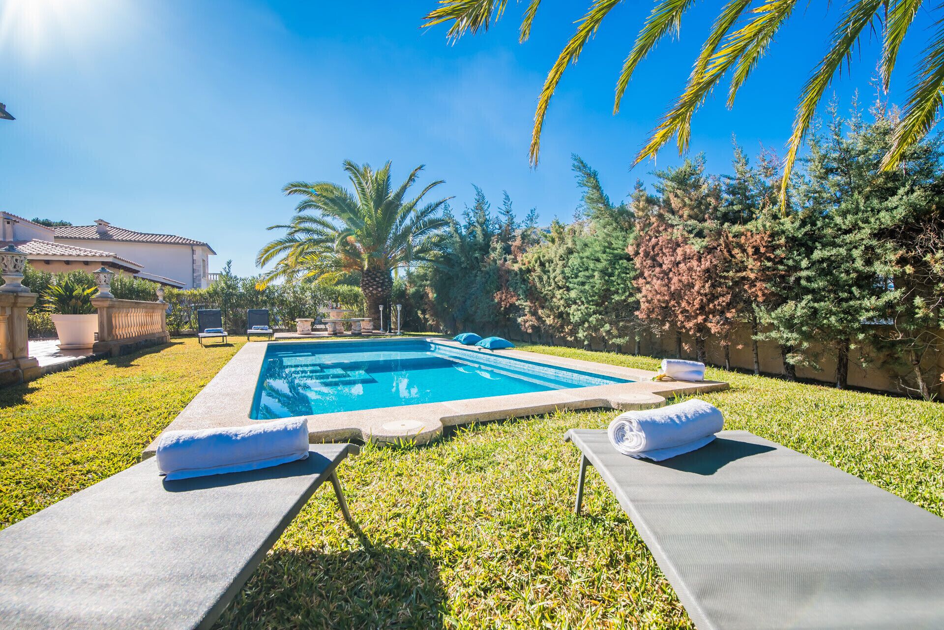 Ein Swimmingpool mit Liegestühlen und Handtüchern, umgeben von Rasen und Bäumen.