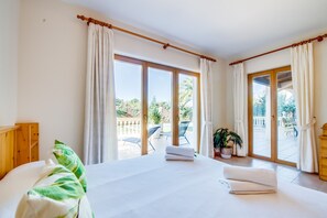 A spacious bedroom with a large bed, two sliding glass doors leading to an outdoor patio, and a wooden headboard. - House in Alcudia Aran Berna with swimming pool (Alcúdia)