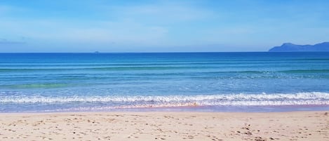 Ein Strand mit Fußabdrücken, die zum Wasser führen, ein klarer Himmel und ferne Berge.