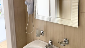 A bathroom with a white sink, a mirror with a window, a hairdryer, and a towel rack. - Giannis Rooms (Chora Sfakion)