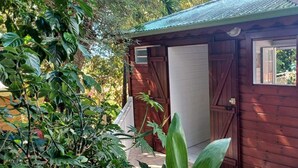 Un abri en bois avec une porte fermée et une fenêtre, entouré d’une végétation luxuriante.