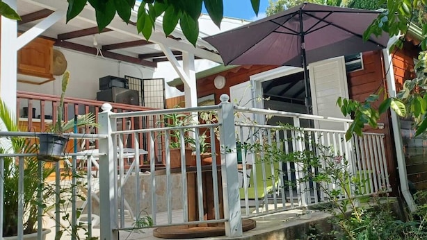 Un espace extérieur abrité, doté d’une balustrade blanche, d’un grand parasol et de plantes en pot.