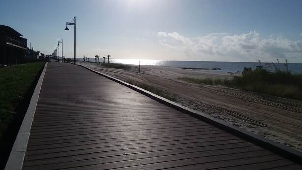 A wooden boardwalk leading to a beach with a clear sky and distant sun. - Amazing Beachview Close to Downtown Entertainment (Biloxi)
