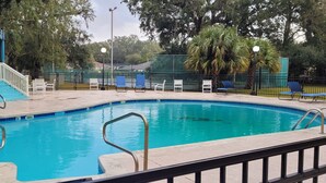 A swimming pool with a blue border, a covered seating area, and a fenced deck with chairs. - Amazing Beachview Close to Downtown Entertainment (Biloxi)
