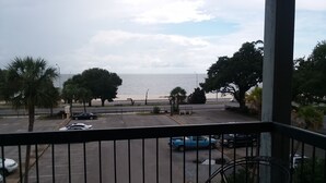 A balcony with a view of the sea, a parking area with several cars, and a table with chairs. - Amazing Beachview Close to Downtown Entertainment (Biloxi)
